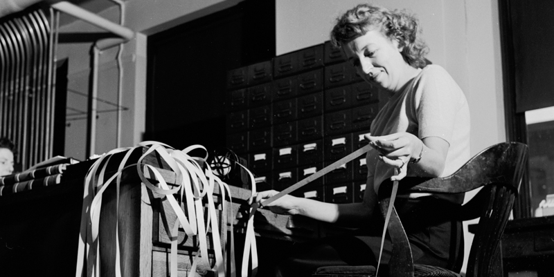 Una impiegata controlla un nastro con le informazioni sui titoli della borsa di New York, negli anni Cinquanta. (Orlando /Three Lions/Getty Images)