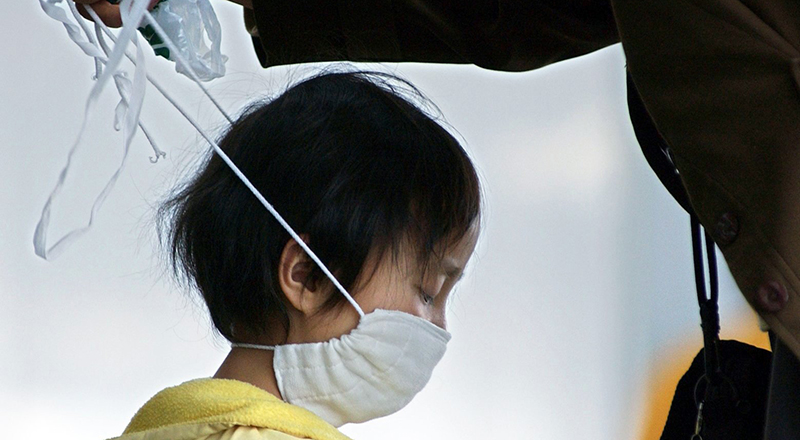 Una bambina viene aiutata a indossare una mascherina all'aeroporto di Pechino, nei giorni della crisi sanitaria legata alla SARS, 22 aprile 2003 (Ken Liu/picture-alliance/dpa/AP Images)