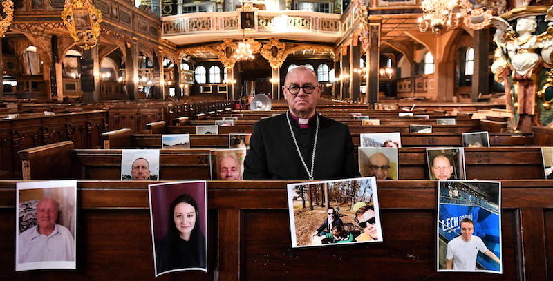 Un sacerdote posa con le foto dei fedeli impossibilitati a partecipare di persona alla messa pasquale per via delle restrizioni per contrastare la diffusione del coronavirus, a Swidnica, in Polonia (EPA/Maciej Kulczynski)