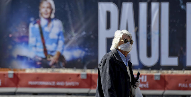 Un passante con la mascherina davanti al manifesto di uno dei due concerti di Paul McCartney previsti in Italia per giugno, cancellati. (ANSA / CIRO FUSCO)