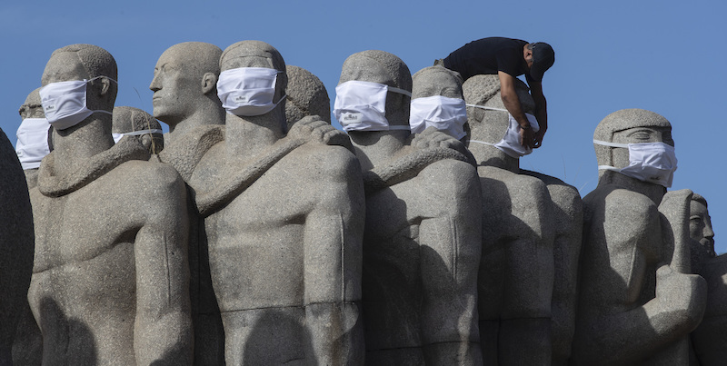 Un uomo mette delle mascherine alle statue di un monumento di San Paolo, in Brasile. (AP Photo/Andre Penner)