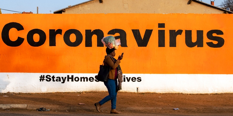 Una donna con la mascherina passa davanti a un cartellone che invita a rispettare le regole per prevenire il contagio da coronavirus. Sudarica, 19 giugno 2020 (Foto AP/Themba Hadebe/File)