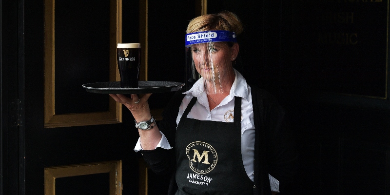 Una cameriera con visiera protettiva porta una pinta di birra al tavolo di un pub di Dublino, il 29 giugno 2020, primo giorno di riapertura dei locali dopo il lockdown (Charles McQuillan/Getty Images)