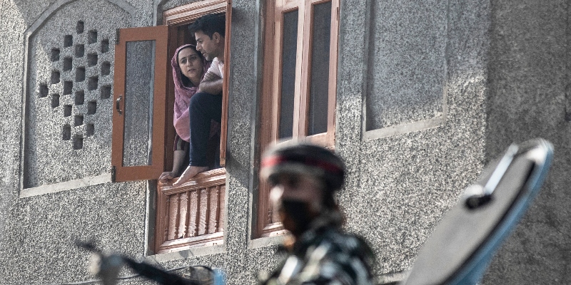 Un paramilitare indiano di guardia su un veicolo blindato mentre una coppia di Srinagar, nel Kashmir, guarda dalla finestra di casa, durante gli scontri del 17 settembre 2020 (AP Photo/Mukhtar Khan)