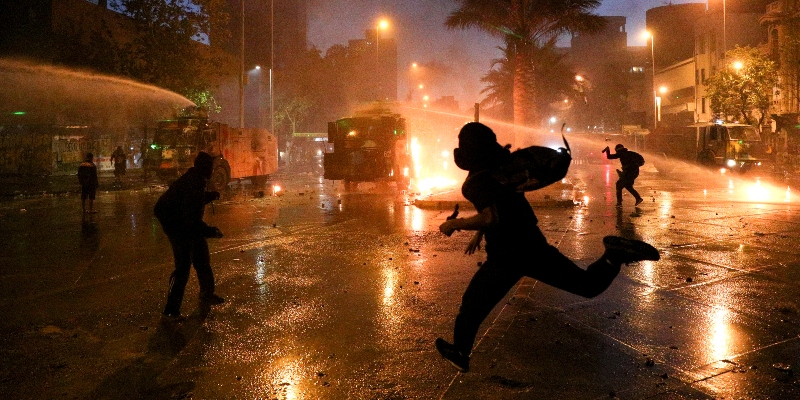 Alcuni manifestanti scappano mentre la polizia cerca di disperderli con gli idranti. Santiago, Cile, 18 ottobre 2020 (AP Photo/Esteban Felix)