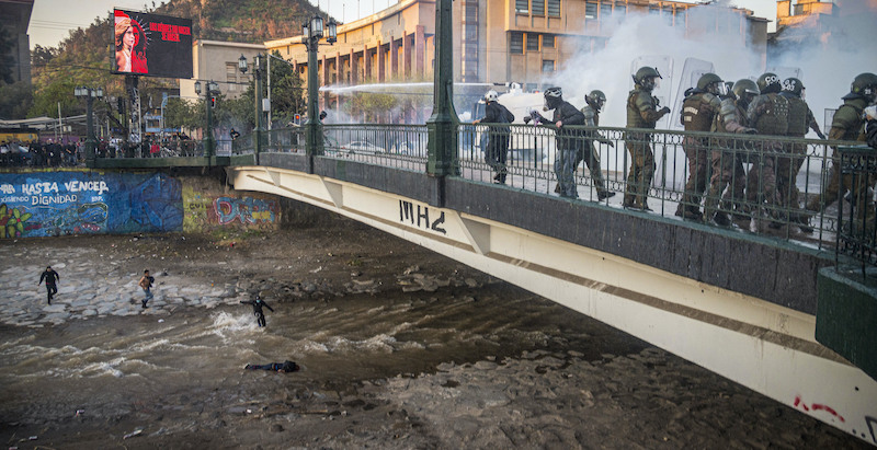 L'adolescente caduto dal ponte, a faccia in giù nel fiume Mapocho, viene soccorso da altri manifestanti (AP Photo/Aliosha Marquez Alvear)