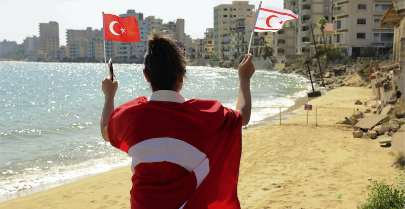 Una donna con la bandiera turca e turca cipriota sulla spiaggia di Varosha, a Cipro Nord (AP Photo/Nedim Enginsoy)