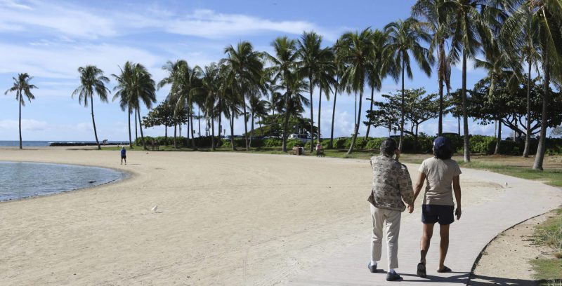 Una coppia di turiste passeggia a Waikiki Beach, a Honolulu, una delle spiagge più note delle Hawaii, lo scorso 2 ottobre. (AP Photo/ Caleb Jones)