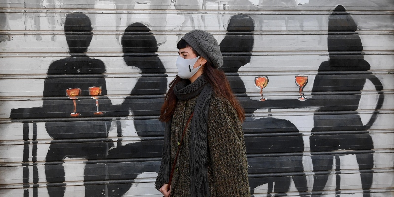 Una ragazza con il volto coperto da una mascherina cammina davanti alla saracinesca abbassata di un locale sul Naviglio Grande su cui è disegnata una scena di persone durante l'ora dell'aperitivo, Milano, 11 gennaio 2021 (ANSA/DANIEL DAL ZENNARO)
