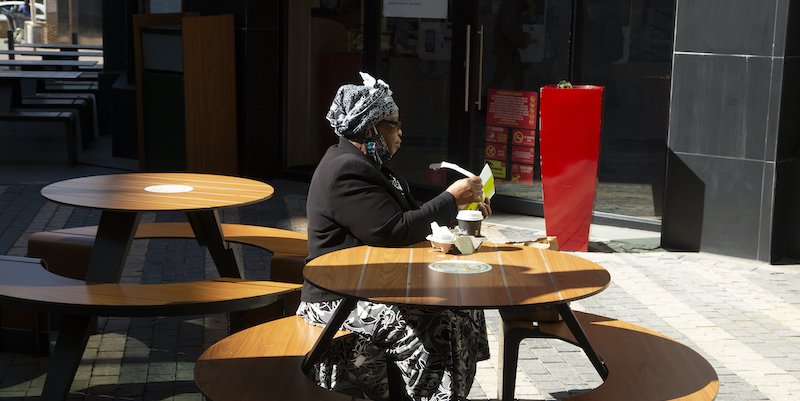 Una donna mangia nei tavoli all'esterno di un fast food a Johannesburg, in Sudafrica, a giugno del 2020, dopo la riapertura dei ristoranti del paese, che erano stati chiusi per 100 giorni a causa del coronavirus (AP Photo/Denis Farrell, LaPresse)