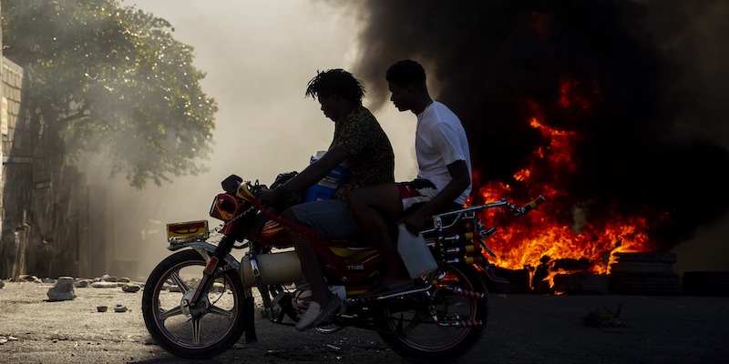 Due uomini su una moto, di fianco a una barricata che brucia a Port-au-Prince, la capitale di Haiti, durante le proteste contro il presidente Jovenel Moïse di domenica 7 febbraio (AP Photo/Dieu Nalio Chery, LaPresse)