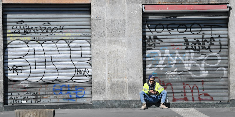 Una persona seduta davanti a un negozio con le saracinesche abbassate a Milano, l'8 aprile 2021. (ANSA/DANIEL DAL ZENNARO)