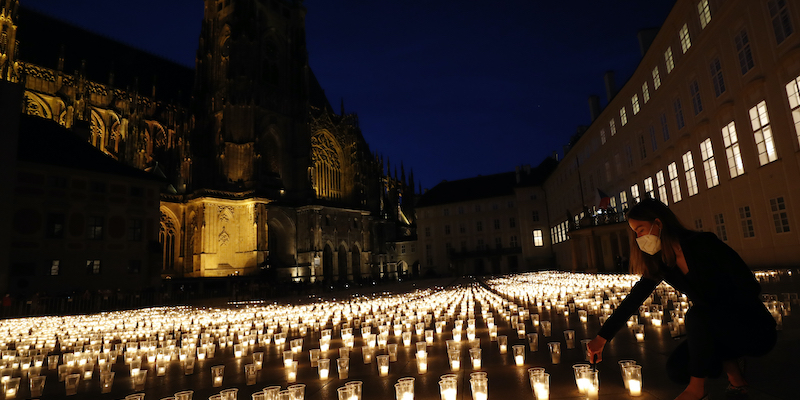 Una donna accende una candela in un sito allestito per commemorare le vittime della pandemia da COVID-19 nel castello di Praga, in Repubblica Ceca, il 10 maggio 2021 (AP Photo/Petr David Josek)