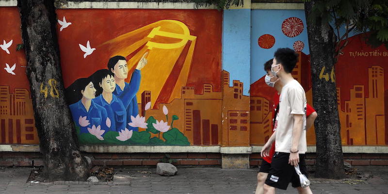 Due ragazzi camminano guardando un murale di propaganda per il Partito comunista vietnamita ad Hanoi, in Vietnam (EPA/LUONG THAI LINH)