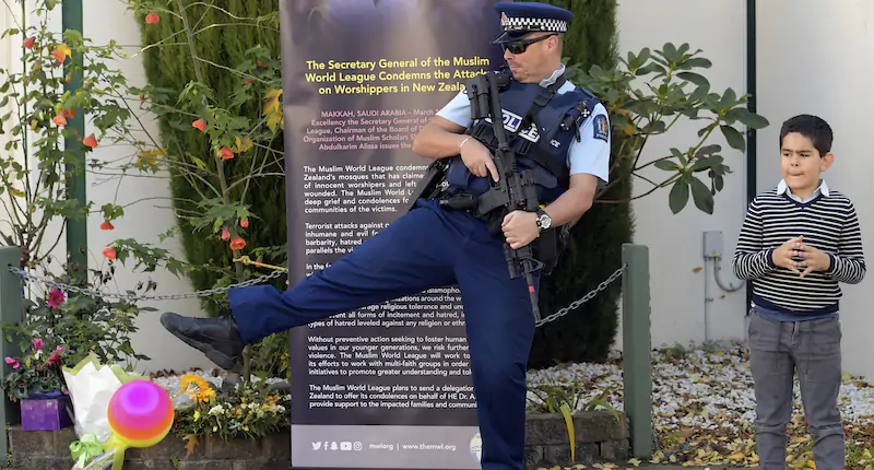 Un poliziotto armato gioca a palla mentre aspetta la visita ufficiale della casa reale inglese a Christchurch, in Nuova Zelanda, dove nel 2018 ci fu un grave attacco terroristico in una moschea e in un centro islamico (Tracey Nearmy/Pool via AP)