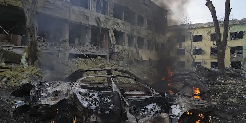 Un'auto carbonizzata e sullo sfondo l'ospedale di Mariupol bombardato (AP Photo/Evgeniy Maloletka)