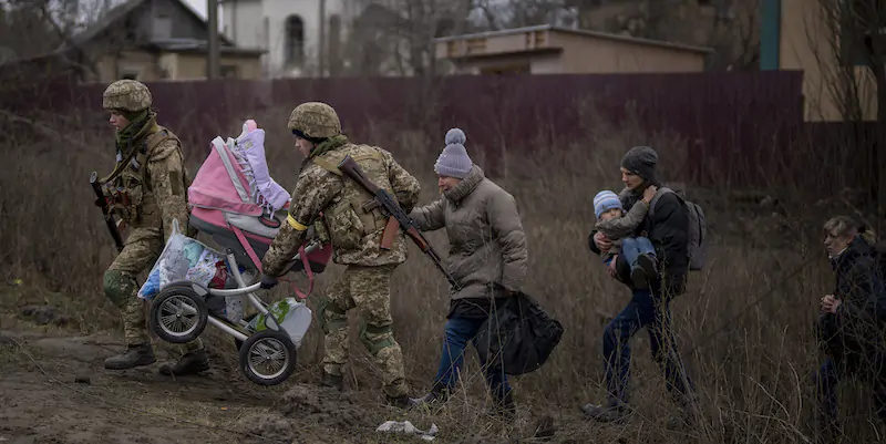 Due soldati aiutano una famiglia ad attraversare il fiume Irpin, per lasciare la città di Kiev (AP Photo/Emilio Morenatti)