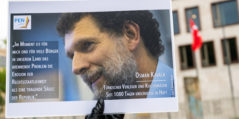 Una persona mostra una foto di Osman Kavala davanti all'ambasciata turca a Berlino, nel 2020 (Christophe Gateau/dpa via ANSA)