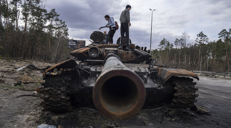 Alcune persone ucraine osservano un carro armato russo distrutto fuori Kiev, ad aprile (AP Photo/Evgeniy Maloletka, File)