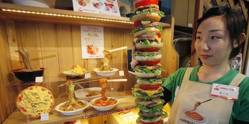 Una dipendente di Iwasaki Be-I mostra una torre di hamburger finti davanti a una vetrina di piatti finti (AP Photo/Koji Sasahara)