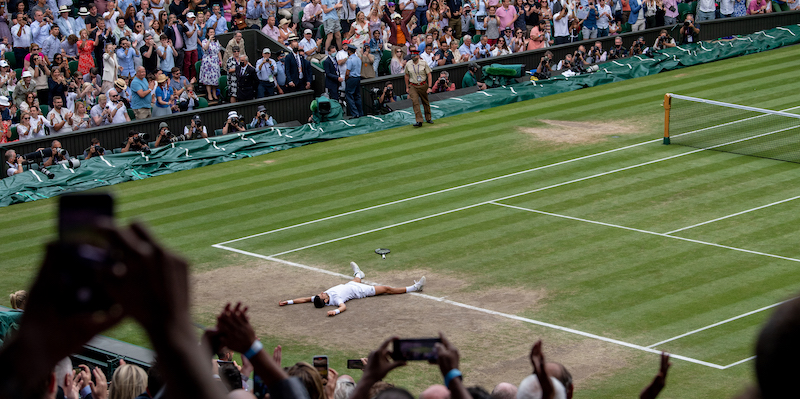 Novak Djokovic si lascia cadere a terra dopo la vittoria a Wimbledon dell'anno scorso, su un prato del campo centrale piuttosto rovinato (AELTC/Florian Eisele via Getty Images)