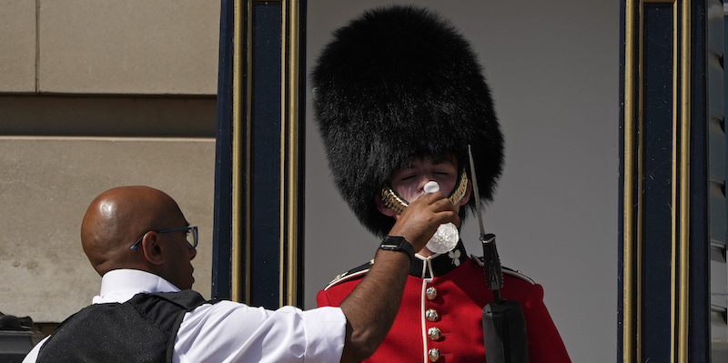Un poliziotto dà da bere a una guardia di Buckingham Palace, Londra, 18 luglio (AP Photo/Matt Dunham)