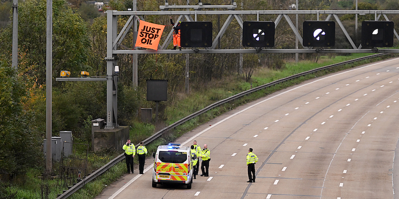 Un gruppo di poliziotti osserva un attivista ambientalista che ha legato un cartellone con la scritta "Just stop oil", "Basta al petrolio", sopra alla M25, l'autostrada che circonda Londra, il 10 novembre 2022 (Leon Neal/Getty Images)
