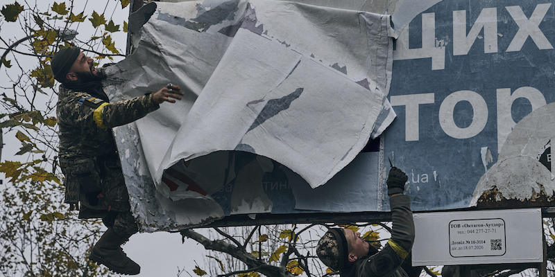 Soldati ucraini che rimuovono alcuni manifesti affissi dai russi a Kherson, il 13 novembre 2022 (AP Photo/LIBKOS)