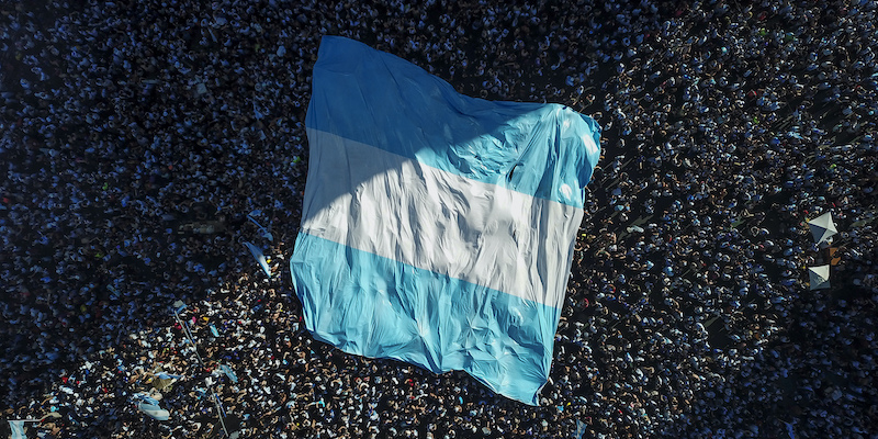 Una bandiera argentina copre la gente in festa a Buenos Aires (AP Photo/Victor R. Caivano)