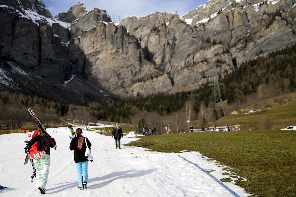 Un gruppo di sciatori su una pista innevata con la neve artificiale in mezzo a prati senza neve