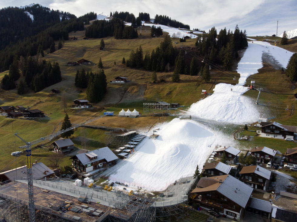 Una pista da sci innevata con cannoni sparaneve, in mezzo a un paesaggio verde e marrone