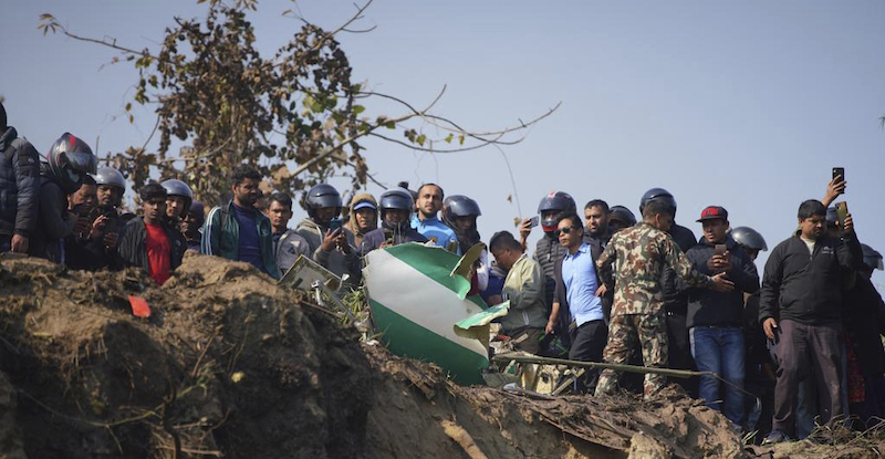 Alcune persone con un rottame dell'aereo caduto in Nepal (AP Photo/Yunish Gurung)