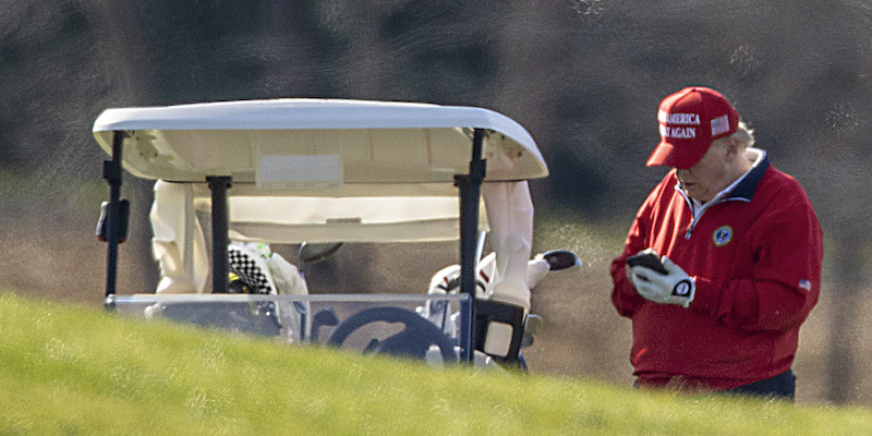 Donald Trump con un telefono in mano in un campo da golf