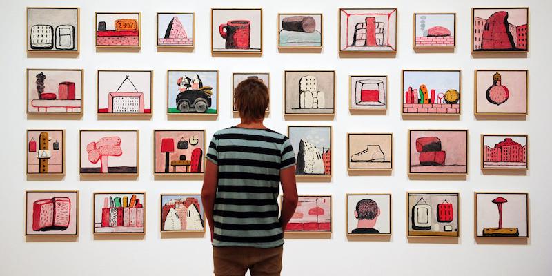 Una serie di piccoli quadri di Philip Guston appesi a un muro e una persona di spalle che li osserva