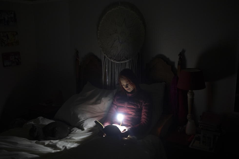 Una donna legge un libro illuminato con una piccola luce a batteria nella sua stanza a Johannesburg