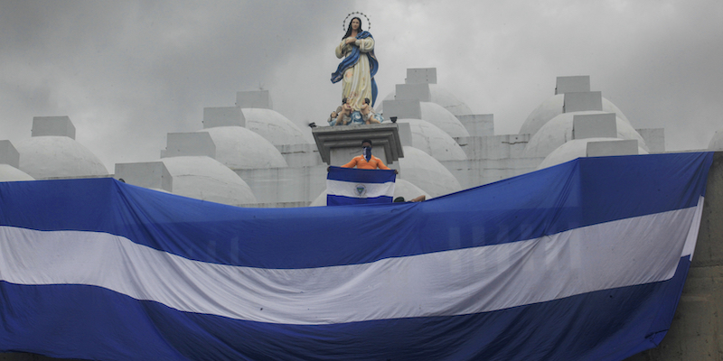 Una grande bandiera del Nicaragua sul tetto della cattedrale di Managua, sotto una statua della Madonna