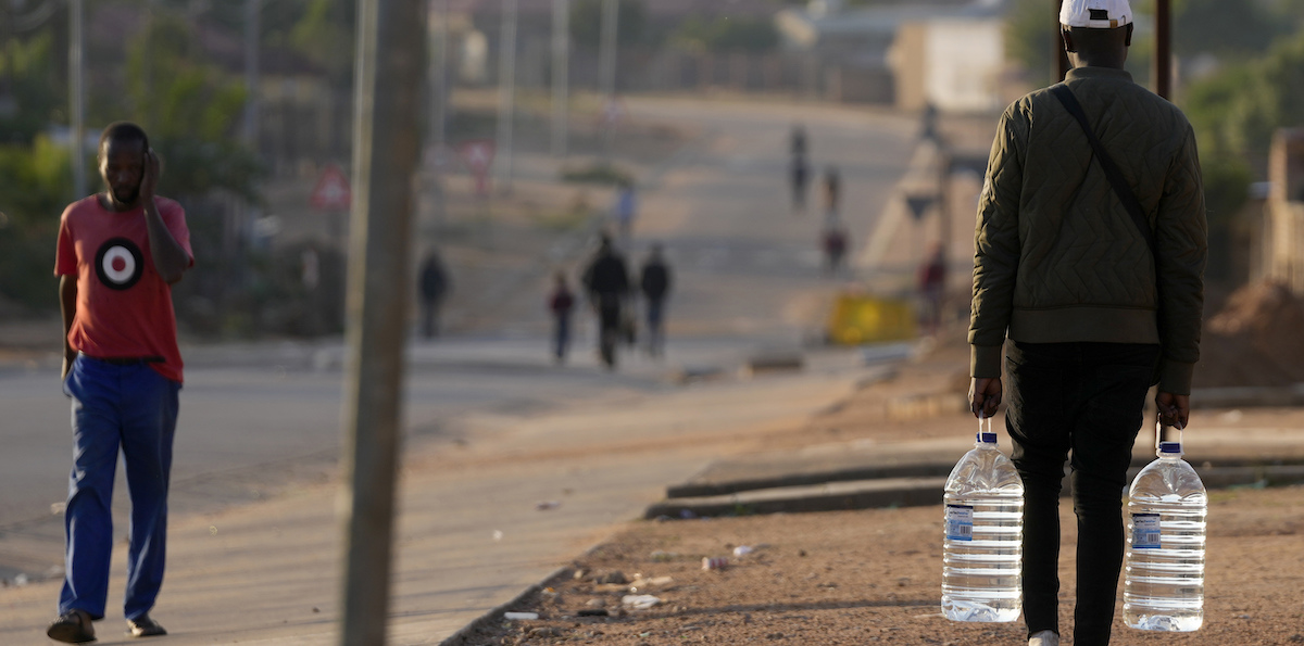 Un uomo con una scorta d'acqua potabile a Hammanskraal, 26 maggio 2023 (AP Photo/Themba Hadebe)