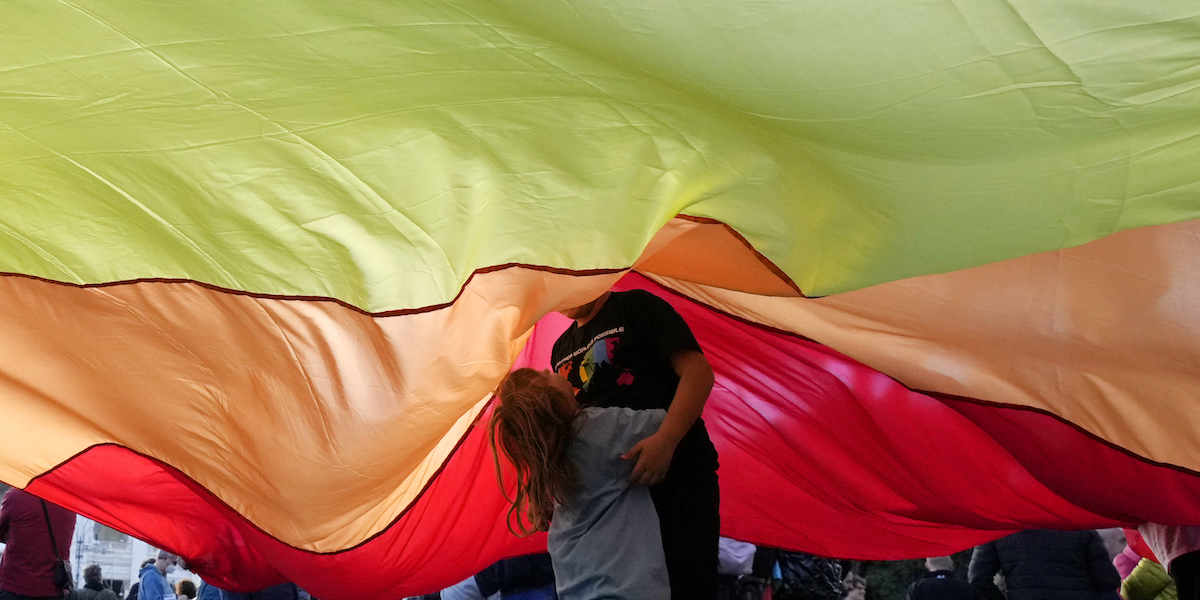 Una bambina gioca con un adulto sotto una grossa bandiera arcobaleno durante il Pride di Roma del 2022 (AP Photo/Gregorio Borgia)