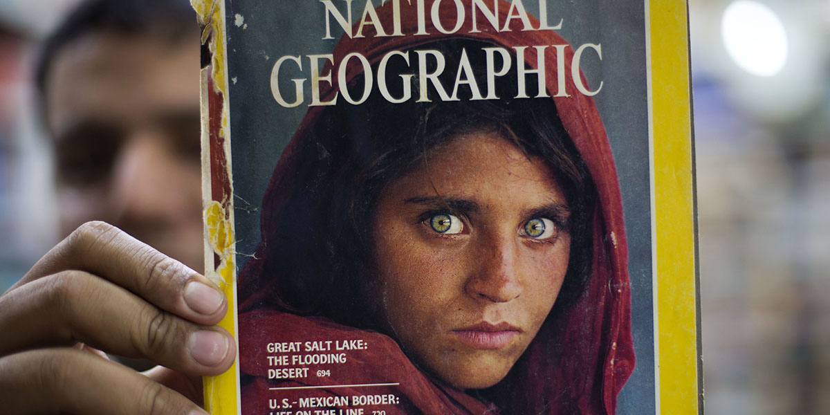 Una famosa copertina del National Geographic con il ritratto della profuga afghana Sharbat Gula del fotografo Steve McCurry, mostrata da un libraio di Islamabad in Pakistan (AP Photo/B.K. Bangash, File)