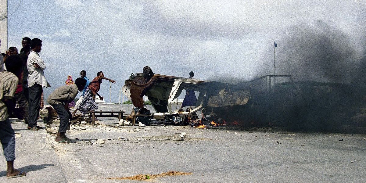 Somali che si riparano dietro una barricata in fiamme e lanciano sassi contro le truppe italiane dell'ONU (AP Photo/Hansi Krauss)