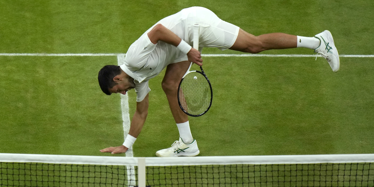 Novak Djokovic tasta l'erba di Wimbledon (AP Photo/Alastair Grant))