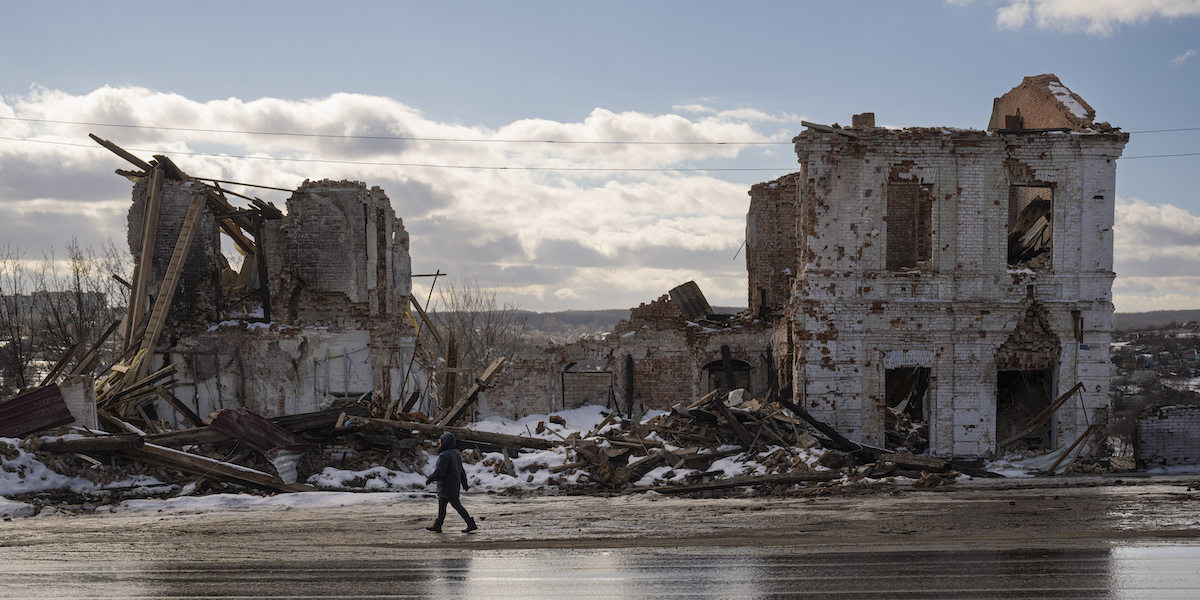 Una donna cammina davanti a un edificio distrutto a Kupiansk il 20 febbraio del 2023
