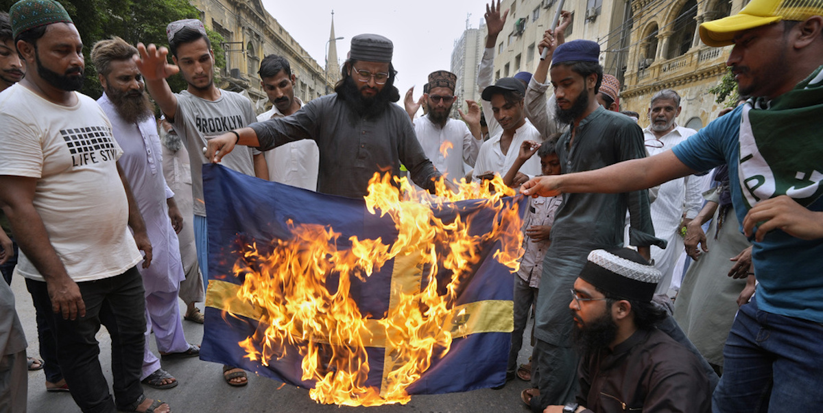 Alcune persone bruciano una bandiera svedese per protestare contro una manifestazione organizzata a Stoccolma a fine giugno in cui era stato bruciato il Corano (AP Photo/Fareed Khan, File)
