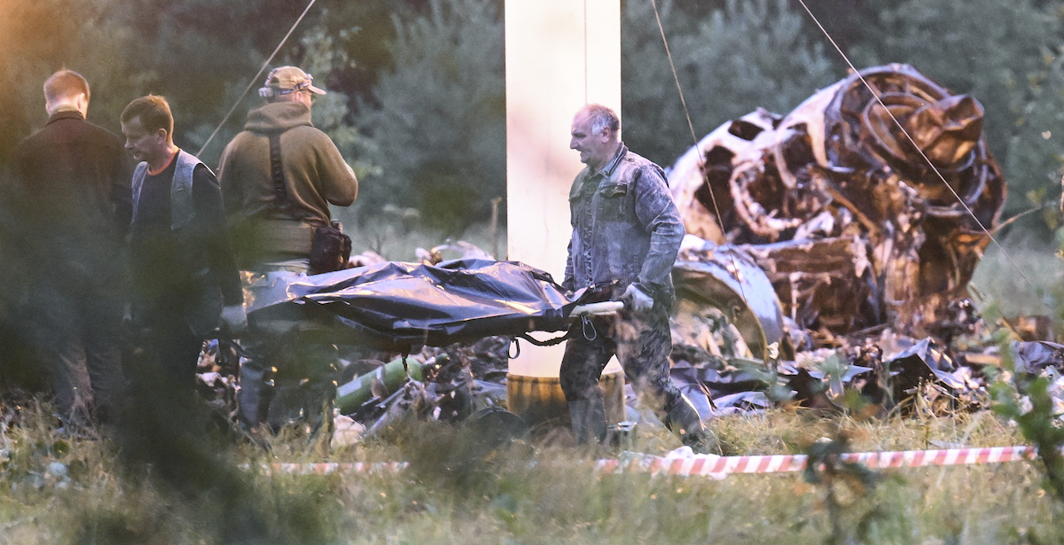 Due persone trasportano un cadavere ritrovato tra i resti dell'aereo di Prigozhin (AP Photo)