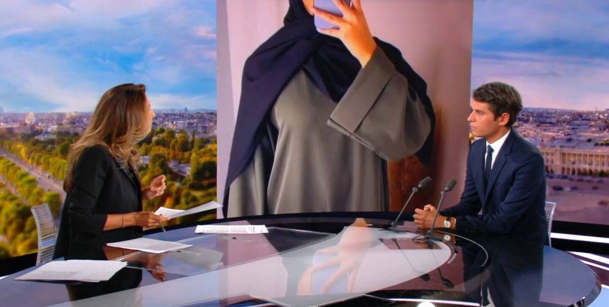 Il ministro francese dell'Istruzione Gabriel Attal intervistato su TF1, e sullo sfondo una foto di una donna con abaya e hijab 