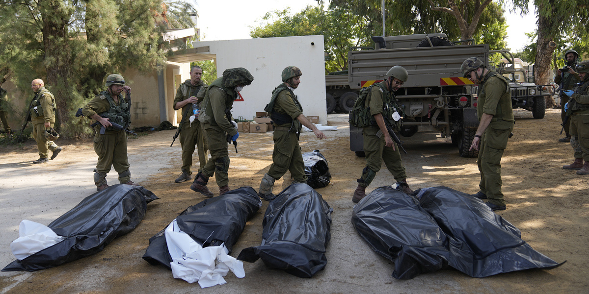Soldati israeliani accanto ai corpi degli israeliani uccisi dai militanti di Hamas nel kibbutz Kfar Azza (AP Photo/Ohad Zwigenberg)