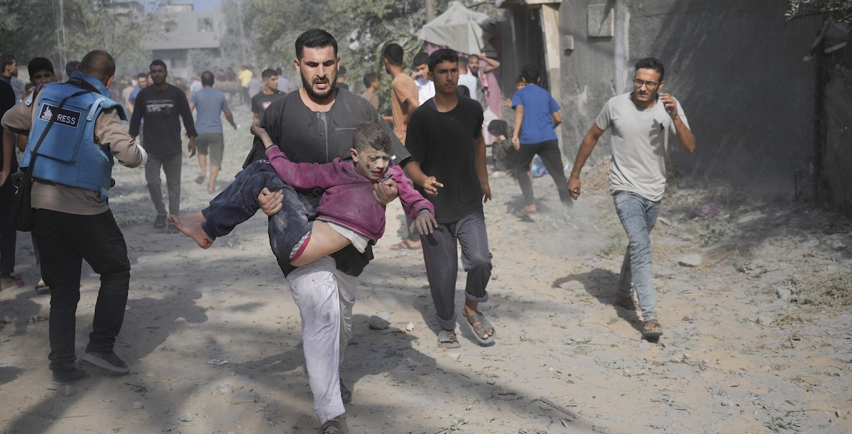 Un uomo palestinese soccorre un bambino ferito a causa di un bombardamento israeliano sulla città di Deir Al-Balah, nella Striscia di Gaza (AP Photo/Hatem Moussa)