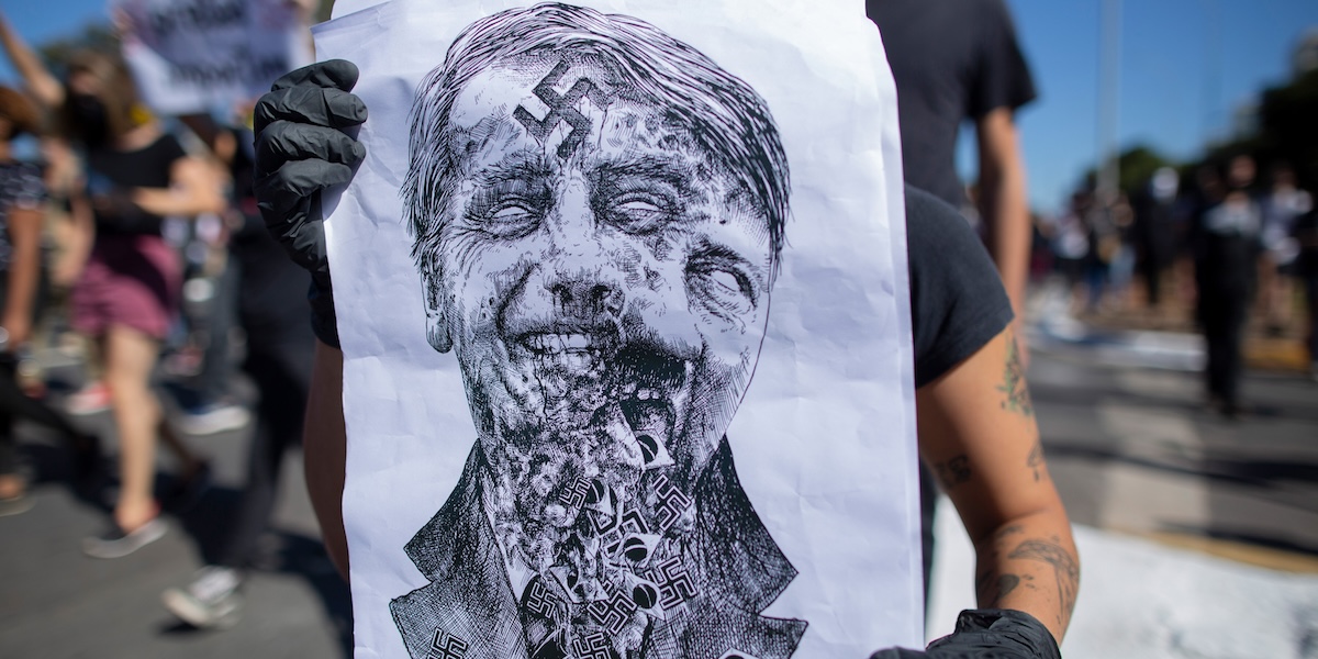 Una persona mostra un poster che sovrappone un ritratto del presidente Jair Bolsonaro a quello di Adolf Hitler durante una manifestazione di protesta nel giugno del 2020 (Myke Sena/ DPA, ANSA)