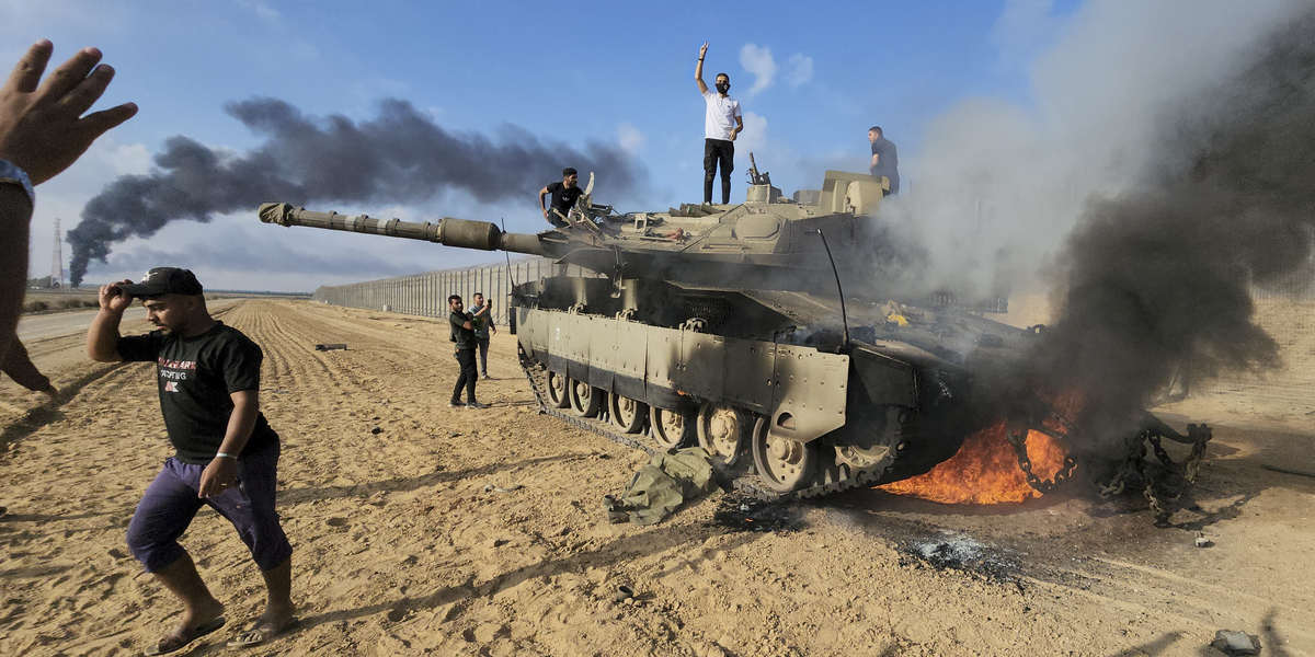 Un gruppo di palestinesi festeggia attorno a un carro armato dato alle fiamme da Hamas il 7 ottobre (AP Photo)