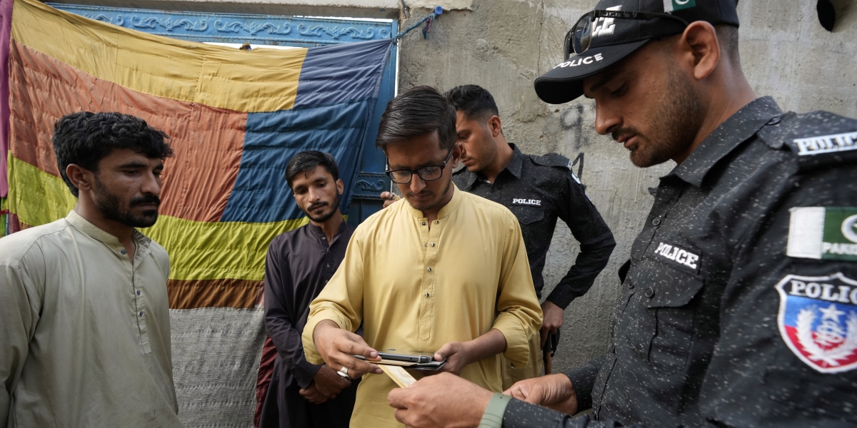 Un poliziotto pakistano controlla i documenti degli abitanti di un quartiere di Karachi (AP Photo/Fareed Khan)